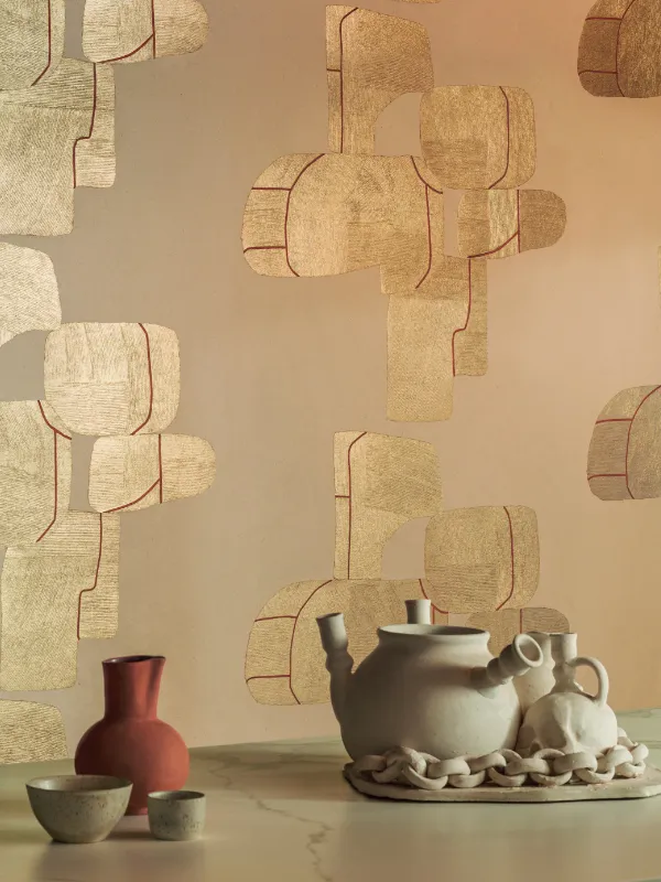 Un papier peint ocre sur lequel sont dessinées des formes dorées avec liseré rouge. Devant une théière en terre cuite.