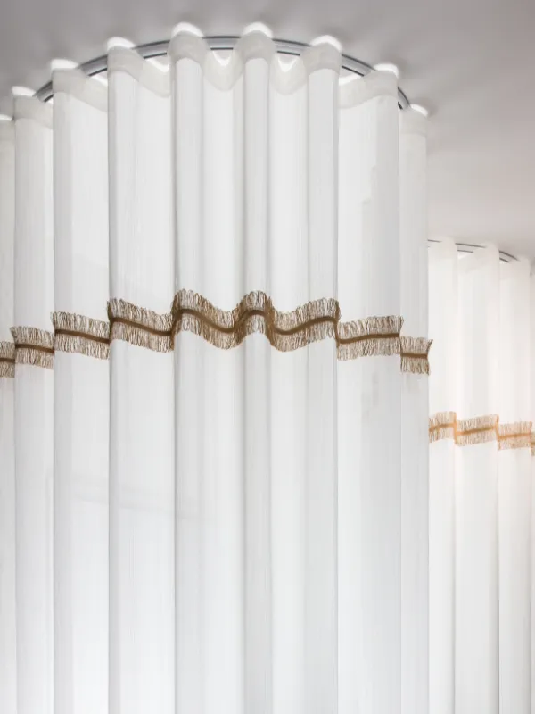 Un rideau sur-mesure en tissus type voilage avec un galon doré et un pli type wave créé par un tapissier décorateur à Metz
